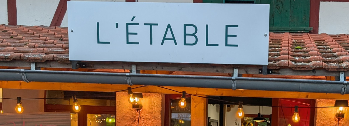 KI generiert: Ein Restaurant mit dem Schild "L'ÉTABLE" und dekorativen Lichtern.
