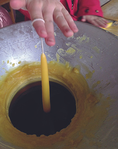 KI generiert: Auf dem Bild sieht man eine Hand, die eine Kerze aus flüssigem Wachs zieht. Der Hauptinhalt des Bildes ist der Kerzenzieherprozess.