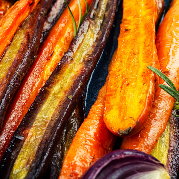 KI generiert: Nahaufnahme von gebratenen bunten Karotten und roten Zwiebeln mit Rosmarin.