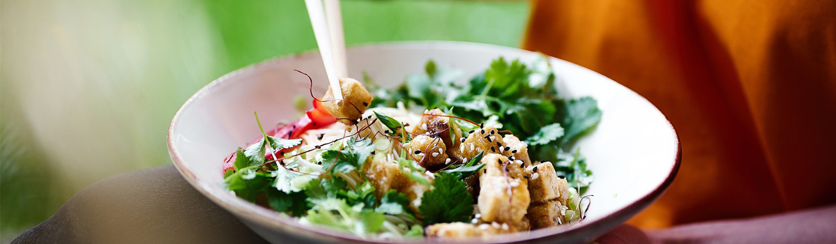 KI generiert: Eine Schüssel mit frischem Salat, Kräutern und Tofustücken, die mit Stäbchen gegessen wird.