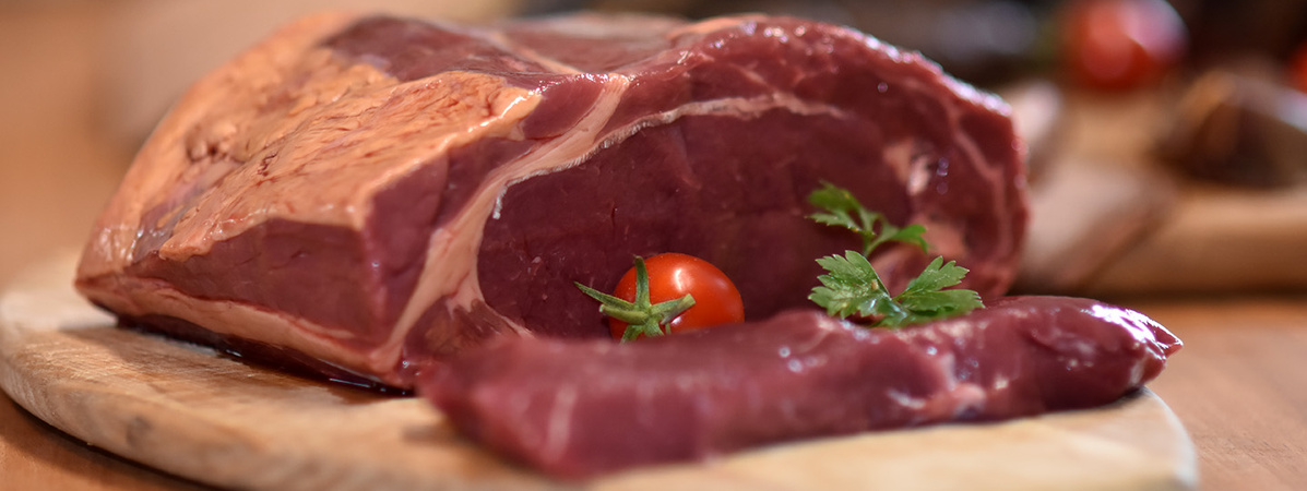 KI generiert: Ein großes Stück rohes Fleisch mit einer Kirschtomate und Petersilie auf einem Holzbrett.