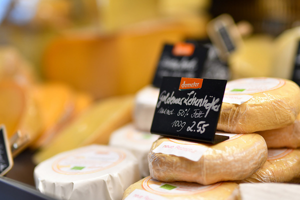 KI generiert: Eine Theke mit verpacktem Käse und einem Preisschild: "Goldener Ziegenkäse, mind. 50% Fett, 100g 2,55".