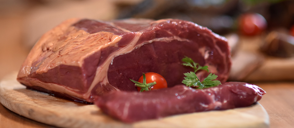 KI generiert: Ein Stück rohes Fleisch auf Holzbrett, dekoriert mit Kirschtomate und Petersilie.