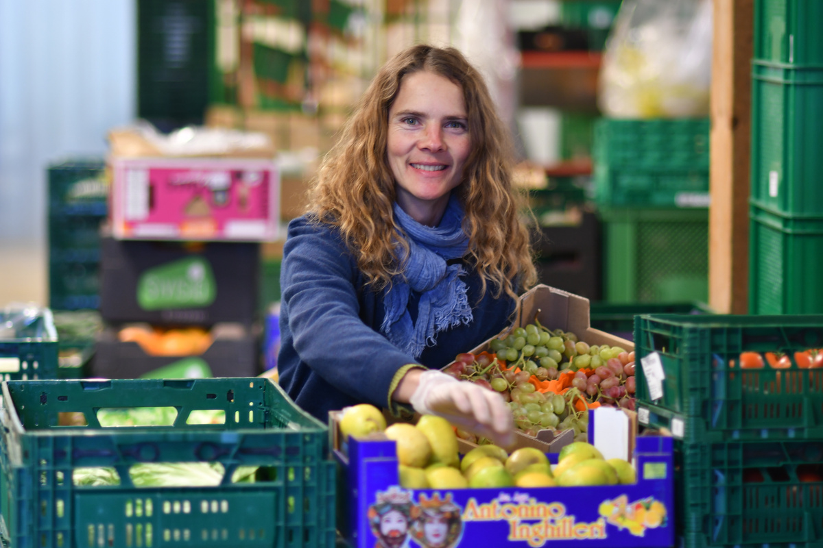 KI generiert: Eine Frau sortiert Obst in einer Kiste, umgeben von weiteren Obst- und Gemüsekisten.