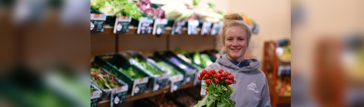 KI generiert: Eine Person hält rote Beeren vor Regalen mit Gemüse in einem Lebensmittelgeschäft.