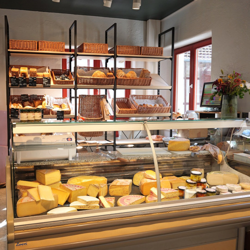 KI generiert: Käsetheke mit verschiedenen Käsesorten und Brotregalen im Hintergrund in einem Laden.