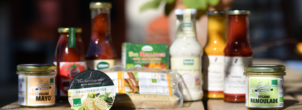 KI generiert: Mehrere Lebensmittelprodukte, darunter vegane Mayonnaise und Remoulade, sind auf einem Tisch angeordnet.